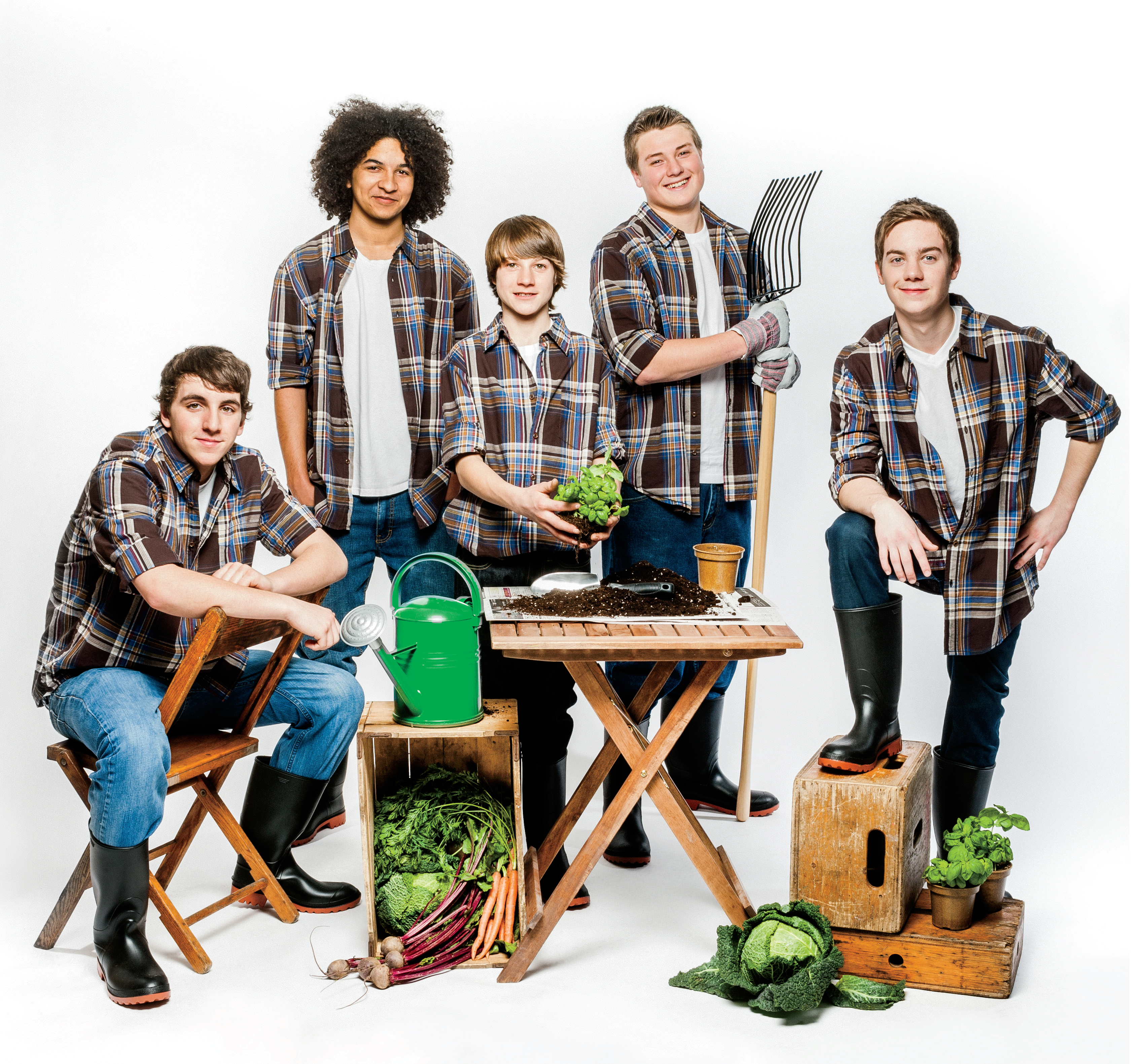 Five teenaged students holding various gardening equipment and vegetables.