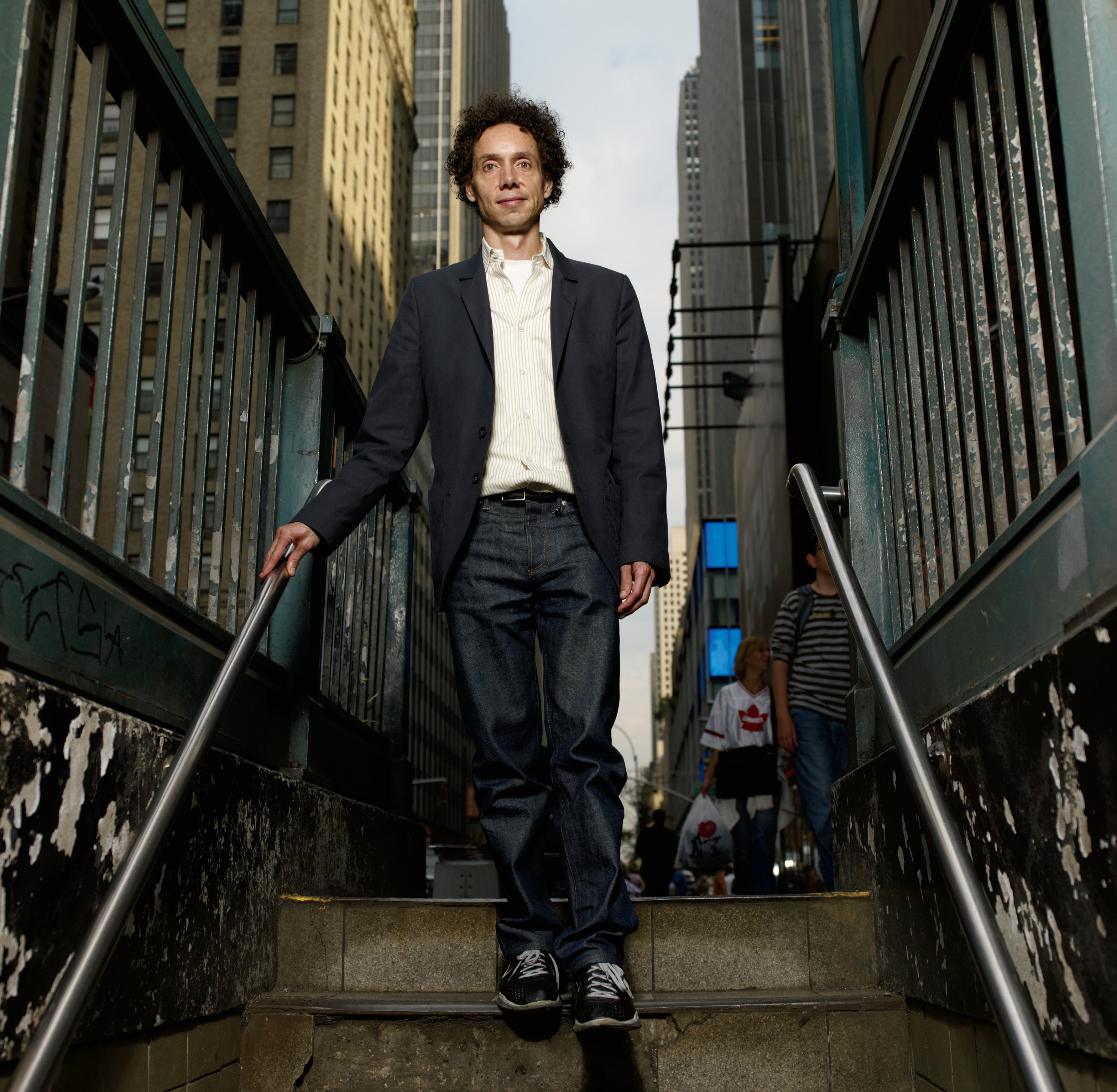 A photo of world-renowned writer Malcolm Gladwell. Malcolm is walking down a set of stairs in the city.