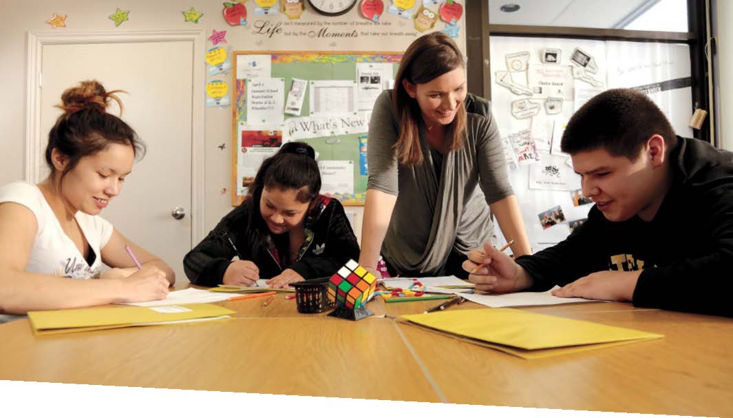 A photo of Samantha Leonard standing over three students. The students are working and Samantha is helping them.