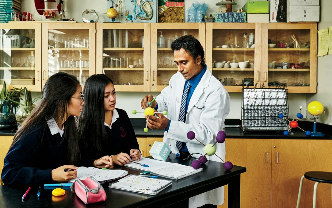 Photo of Gabriel Ayyavoo holding a model of a molecule. Gabriel is discussing the composition of this molecule to two students.