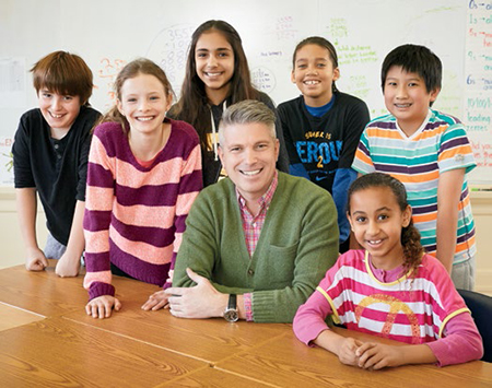 Photo of College Registrar Michael Salvatori seated at a table. Michael is surrounded by smiling young students.
