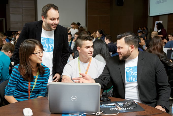 Joseph Romano and Brandon Zoras seated at a table with two students working on a computer.