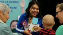 A photo of a smiling College staff member greeting a baby and parents at the London Baby Expo.