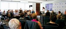 A photo of College Chair Angela De Palma standing at a podium in front of a packed room.
