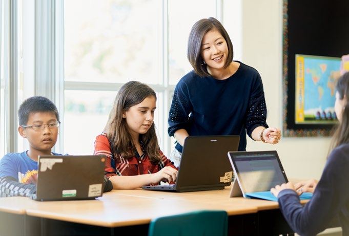 A photo of Yvonne Sun-Hsu helping a student with a laptop. There are two other students nearby working on laptops.
