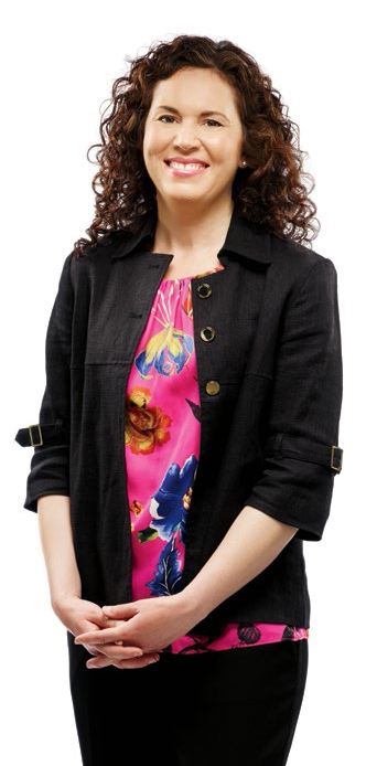 A photo of College Chair Angela De Palma standing with hands clasped. Angela is smiling.