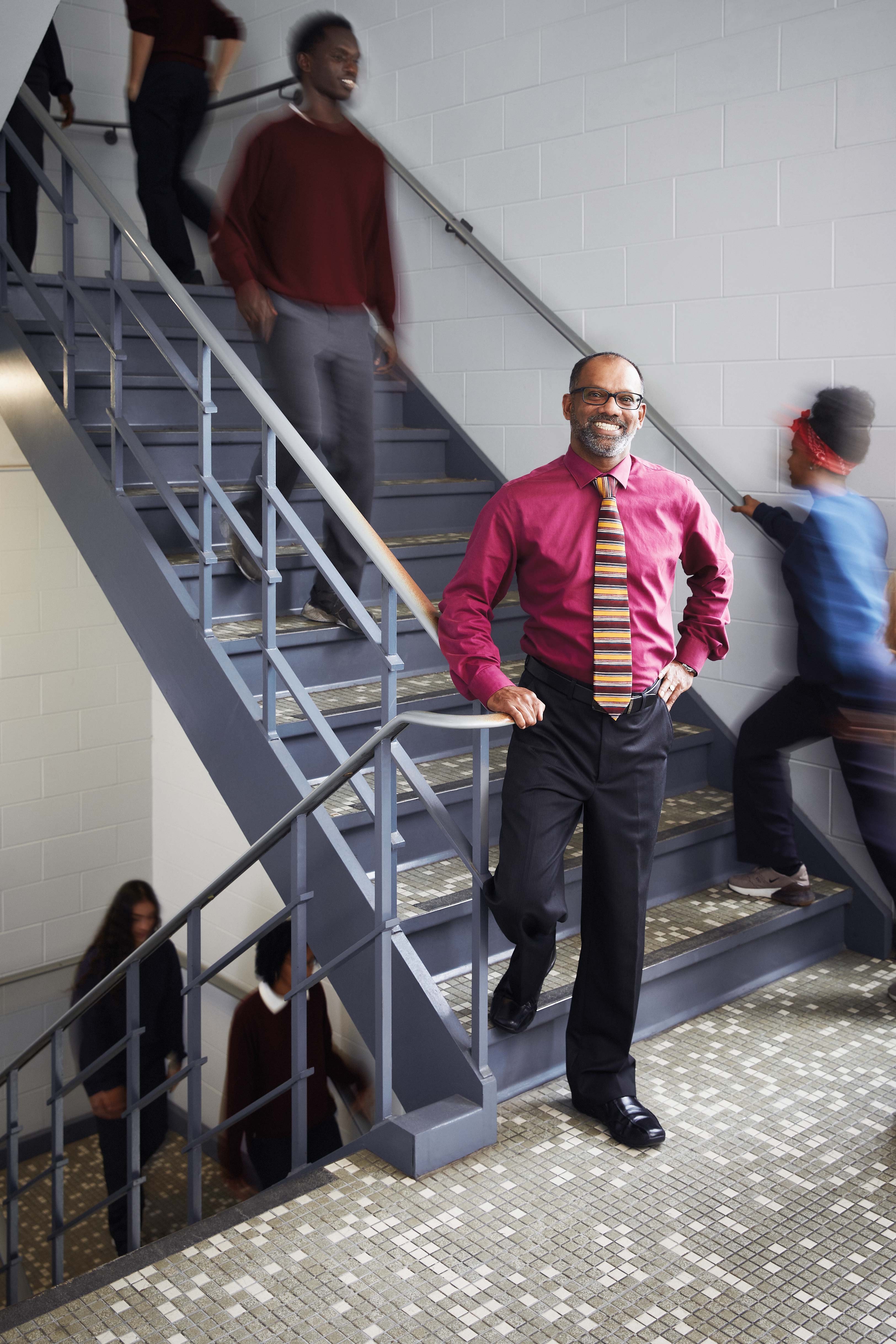 Photo of Michael Naicker, Ontario Certified Teacher, standing in a stairwell while students walk in the background.