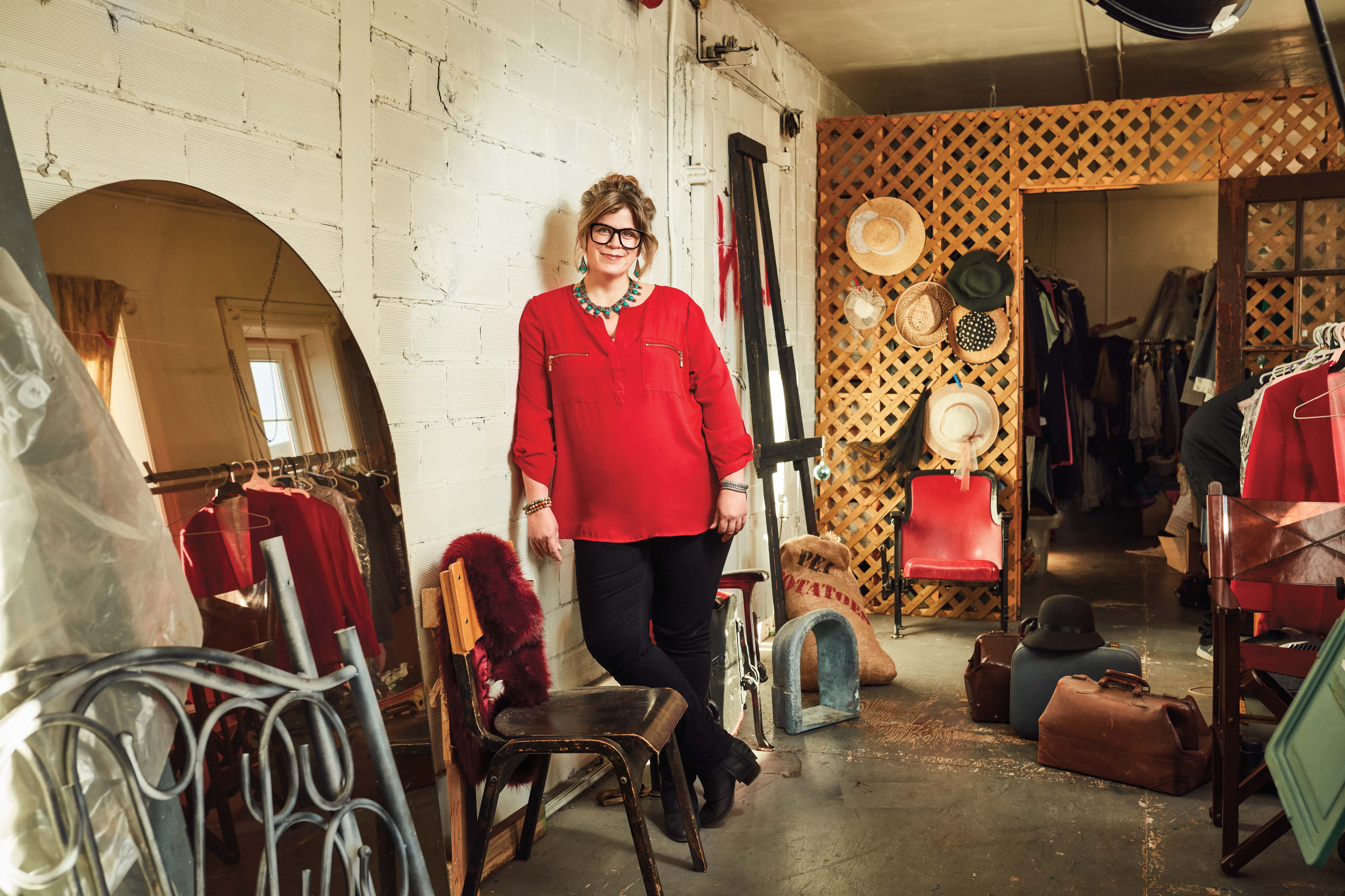 Photo of Jessica Kennedy, Ontario Certified Teacher, leaning against a wall. Jessica is surrounded by costumes and props used for theatre shows.