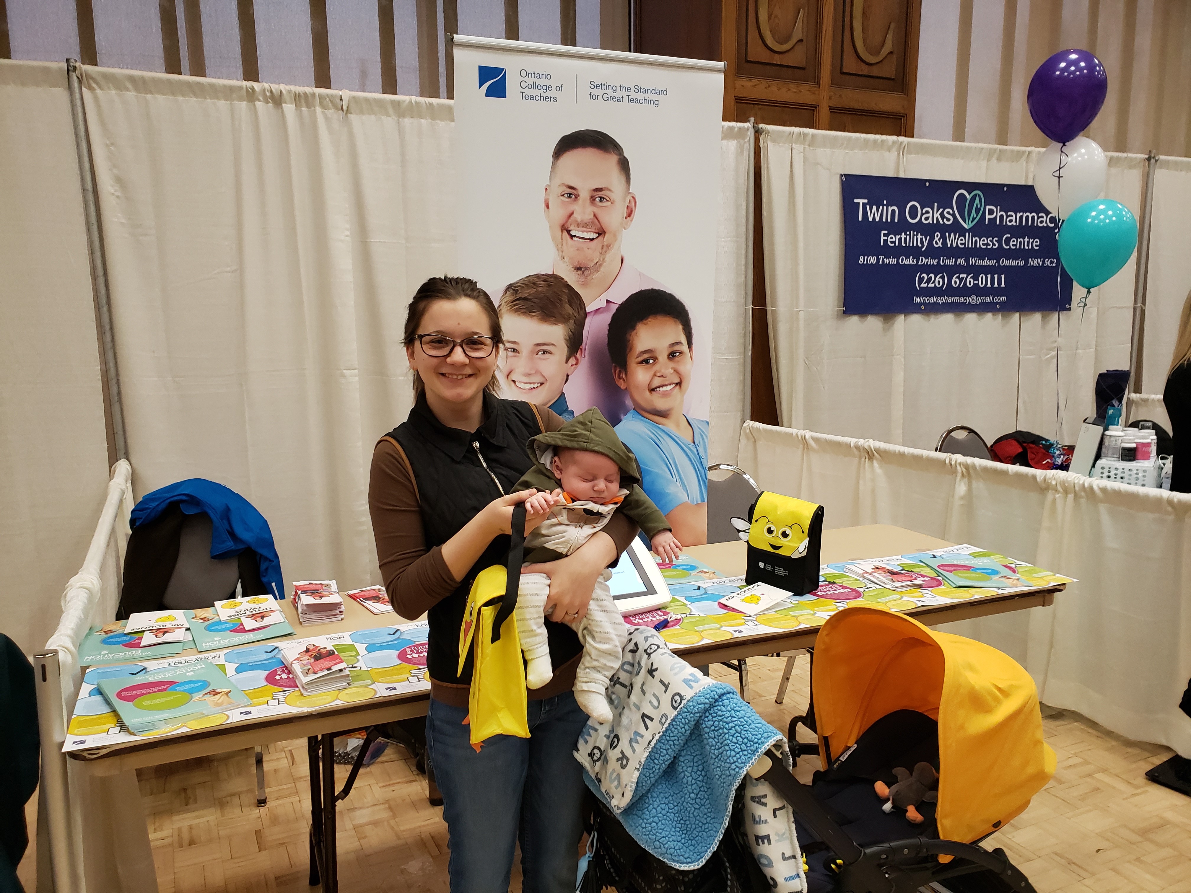 Photo of a person holding a baby. Behind them is an Ontario College of Teachers banner.