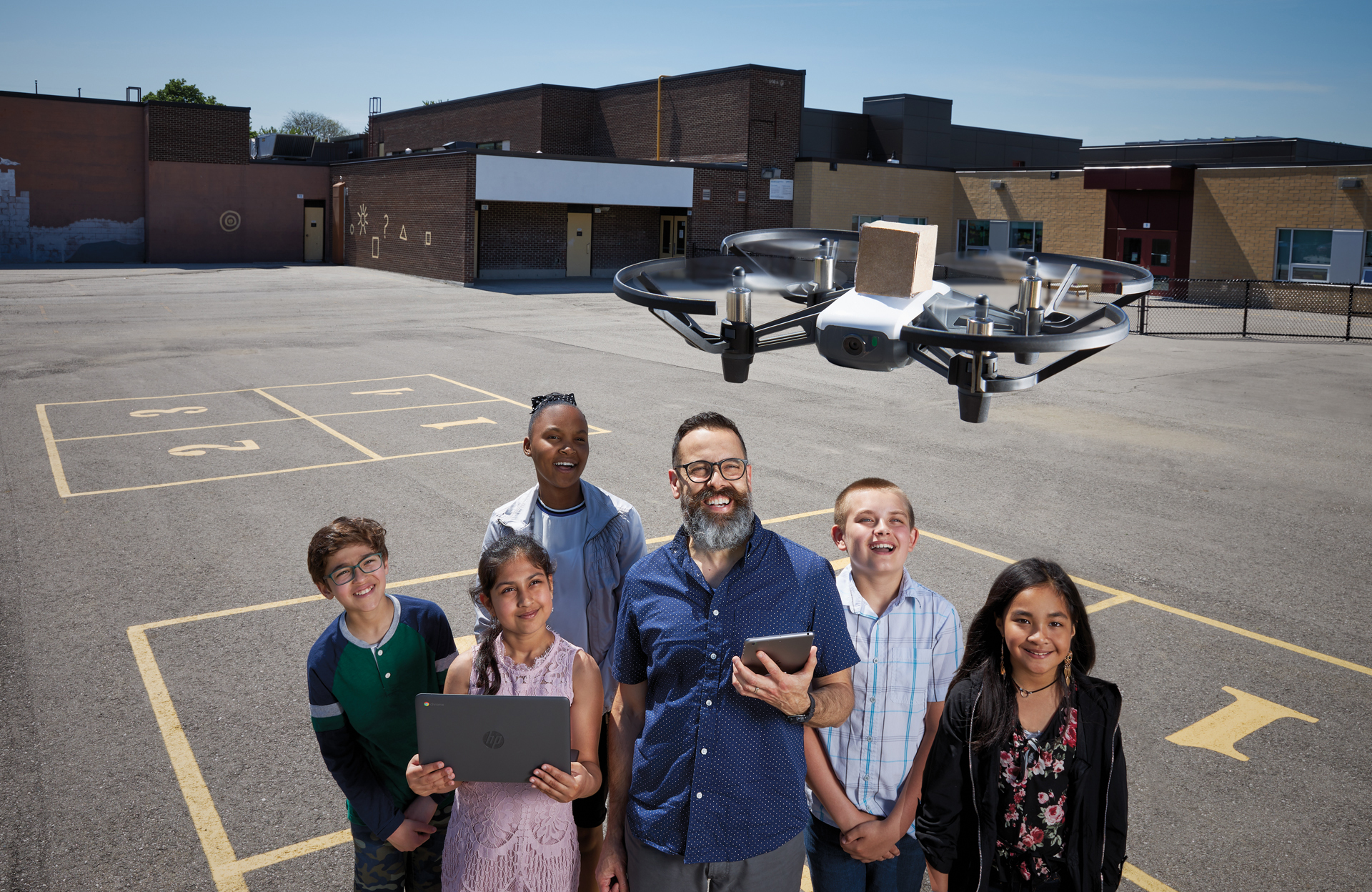 Photo of Antonio Saccucci, Ontario Certified Teacher, outside in the school playground with five students. All are smiling. There is a drone hovering over their heads.