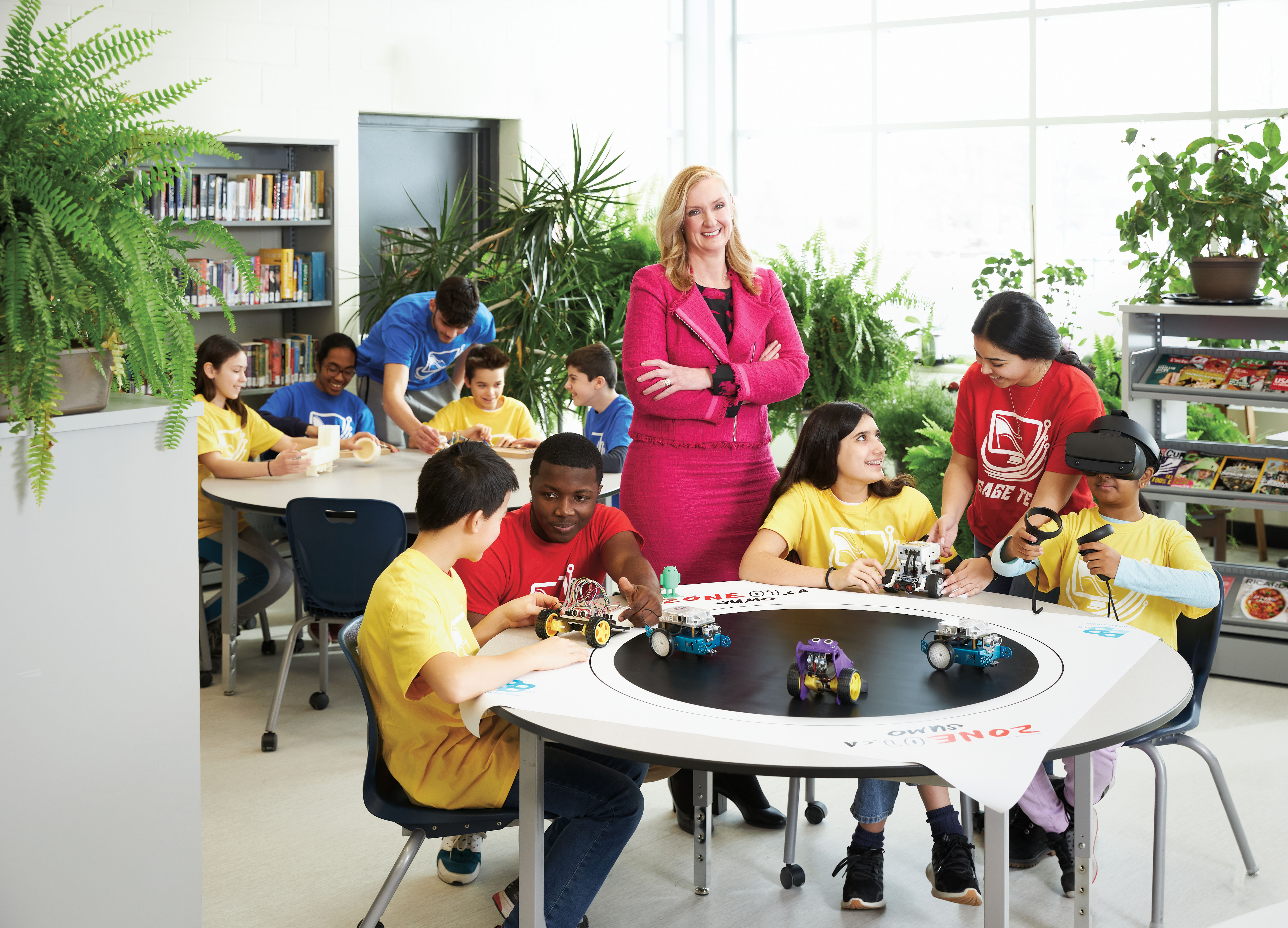 Photo of Josée Landriault, OCT, smiling in a suit with arms crossed. Josée stands in between two tables in a classroom with students sitting and standing.