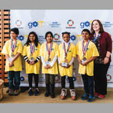 Photo of Laura Kerpel, OCT, a Grade 3 teacher at Cedar Drive Junior Public School, smiling with students who are wearing award medals around their necks.
