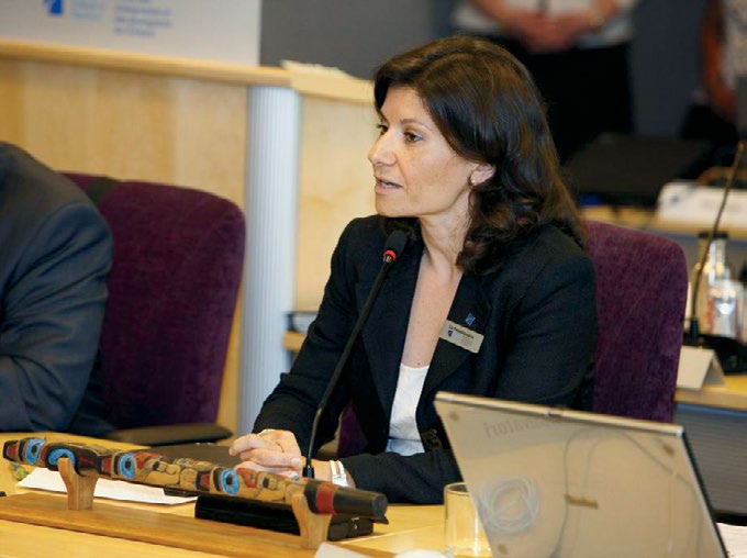 Photo of College Chair Liz Papadopoulos seated at a desk and speaking into a microphone.