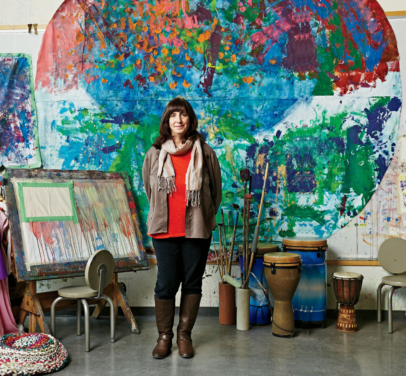 A photo of Renee Hiltz, Ontario Certified Teacher, standing in front of a wall decorated with paint splotches. Behind Renee are a canvas and bongo drums.