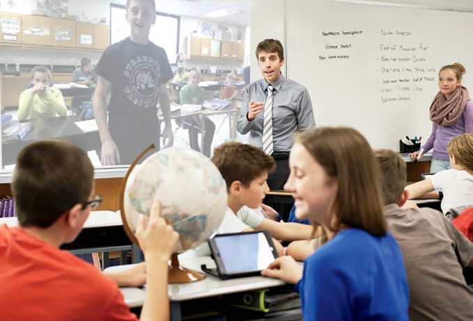 A photo of Joe Grabowski pointing at two students in the foreground. One of the students in the foreground is pointing at a globe.