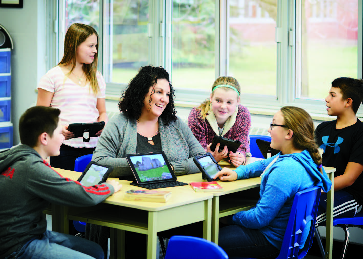 Joey Jackson, Ontario Certified Teacher, sits with a group of students. They are all using tablets.