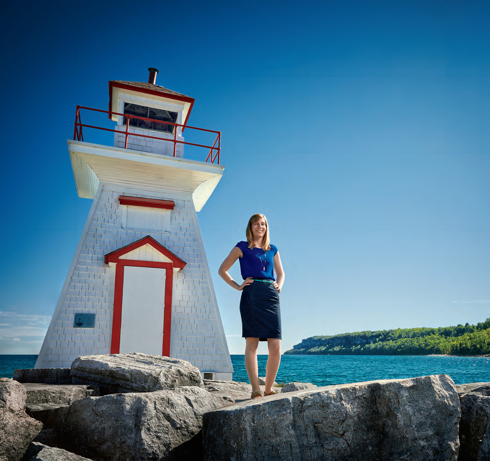 A photo of Breanna Myles standing in front of a small white lighthouse. Breanna is smiling.