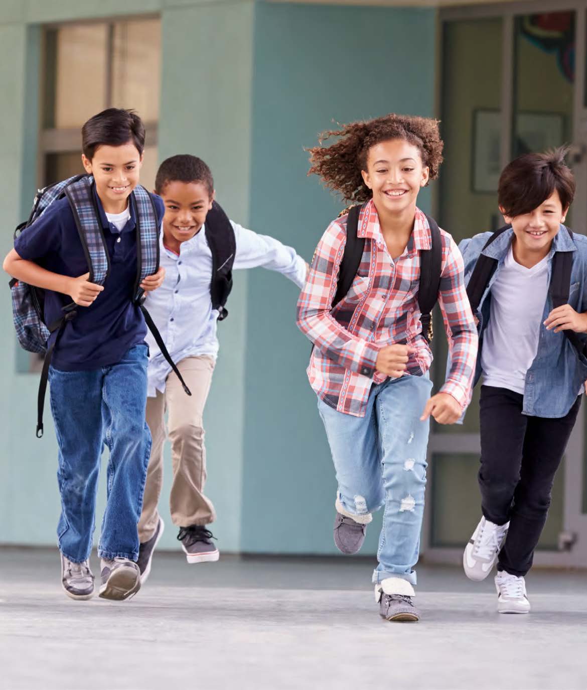 Photo of a group of smiling young students running together. Each of the students is wearing a backpack.