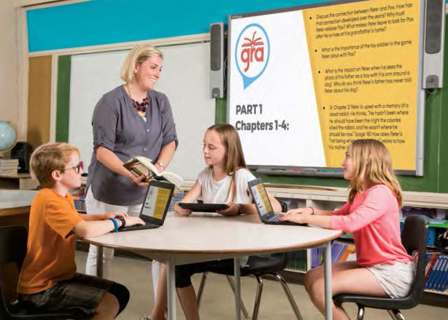 Photo of Caroline Thuss standing at a table where three students are seated.