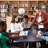 Photo of Denise Salsman, Ontario Certified Teacher, in the library engaging with students using tablets.