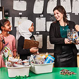 Photo of Rebecca Chahine, Ontario Certified Teacher, smiling at students helping in the classroom. There are tubs filled with classroom waste.