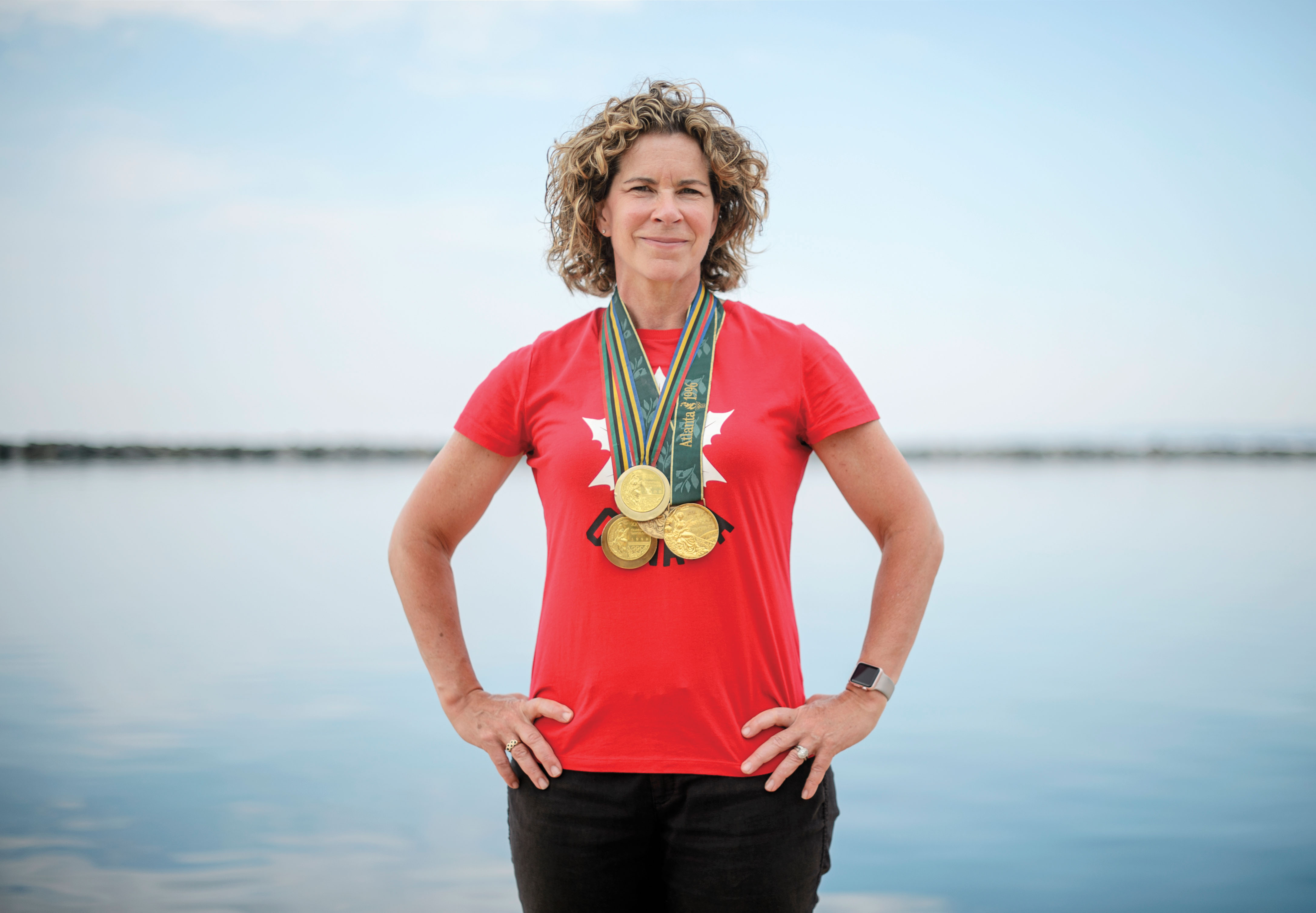 Photo of Summer Olympics gold medalist Marnie McBean smiling with several gold medals around her neck and hands on her hips.